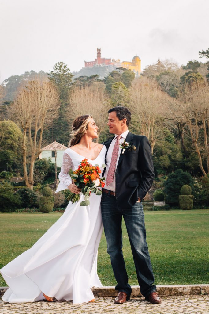 noivos em pé com o palácio da pena no fundo