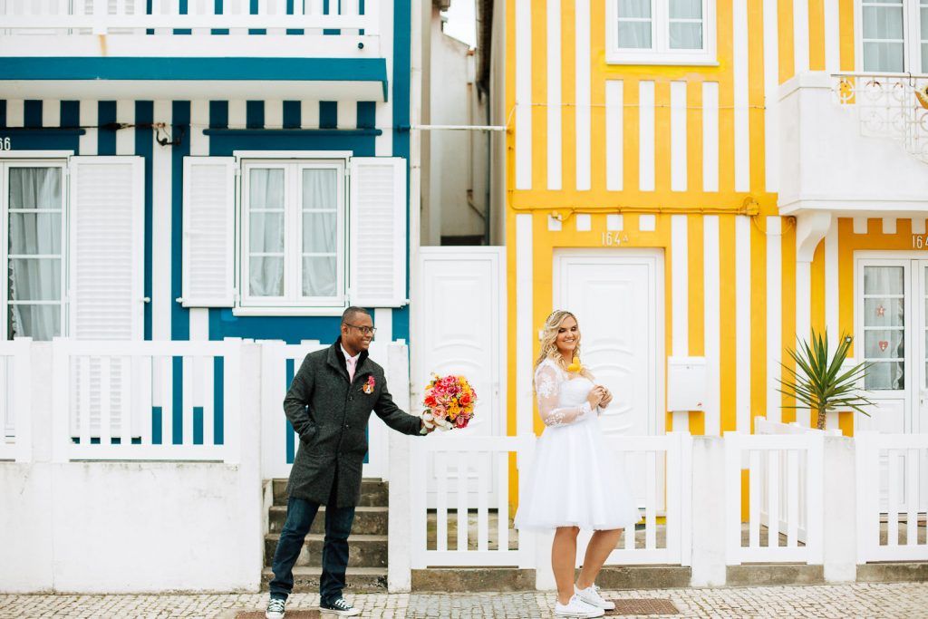 noivo dando o buquê a noivo no fundo de casas coloridas