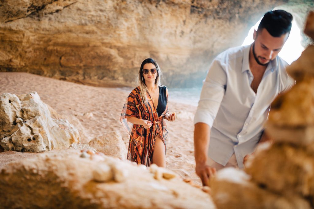 ensaio gruta benagil ela atrás dele olhando ele criando um coração de conchas
