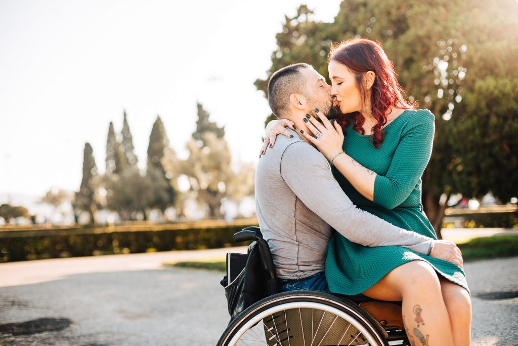 noiva sentada no colo do noivo na cadeira de rodas e se beijando em um parque de Lisboa Portugal
