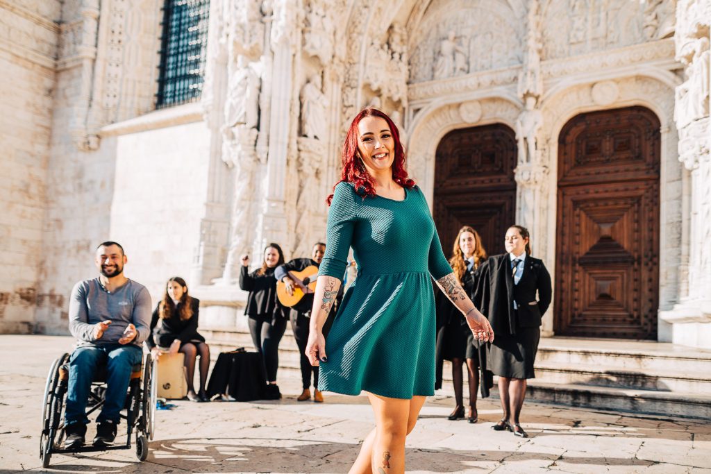 noiva dançando e noivo na cadeira de rodas batendo palmas com algumas estudantes cantando e tocando em frente ao Mosteiro dos Jeronimos