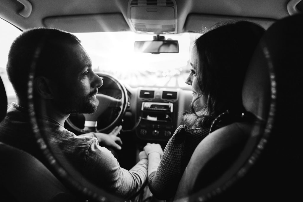 foto preto e branca do casal se admirando dentro do carro com o noivo ao volante e ela de passageira
